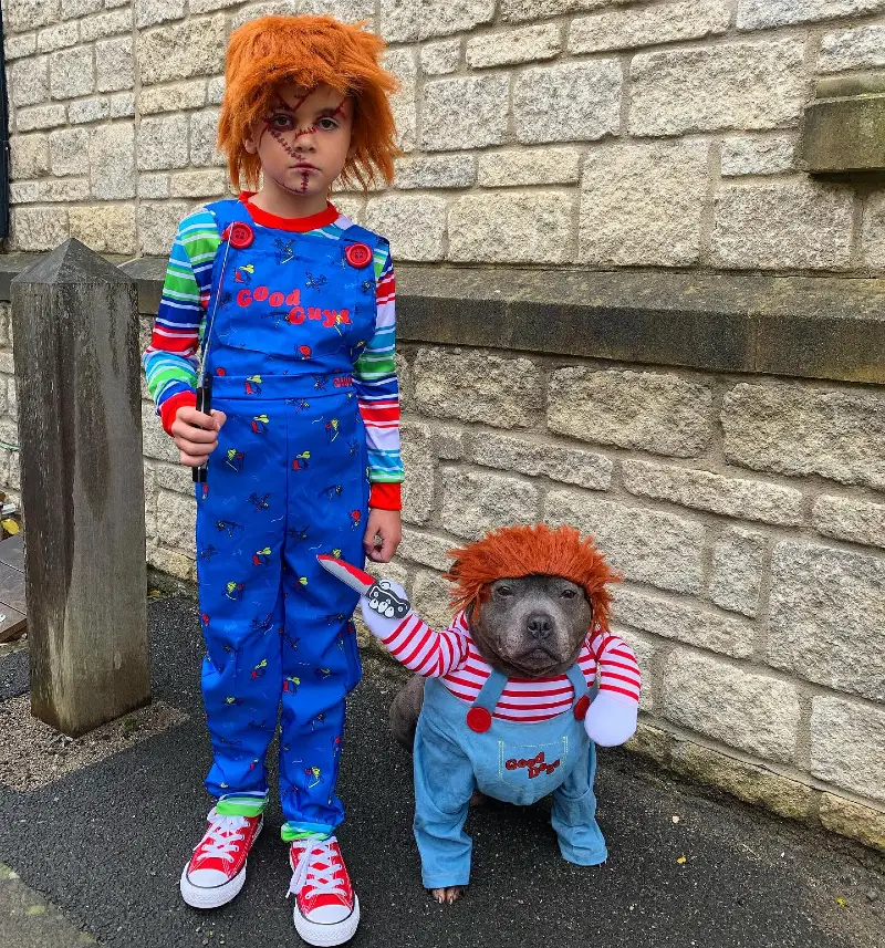 8. Chucky-Inspired Matching Costume with “Good Guys” Kid and Dog Duo by Stone Wall