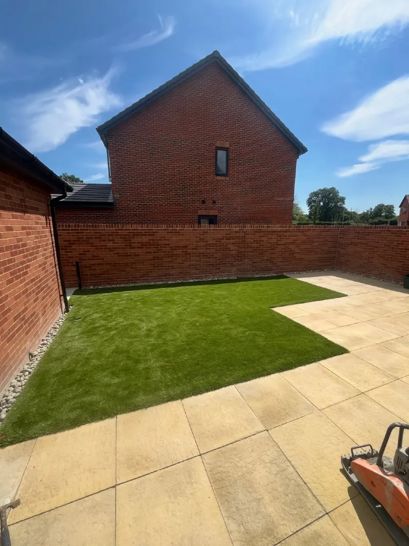 Artificial Turf Patch with Tan Stone Pavers and High Brick Boundary Wall