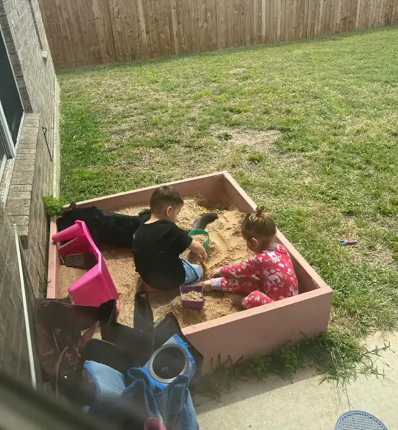 Dusty Pink Painted Wooden Sandbox Positioned Against a Tan Brick Exterior Wall