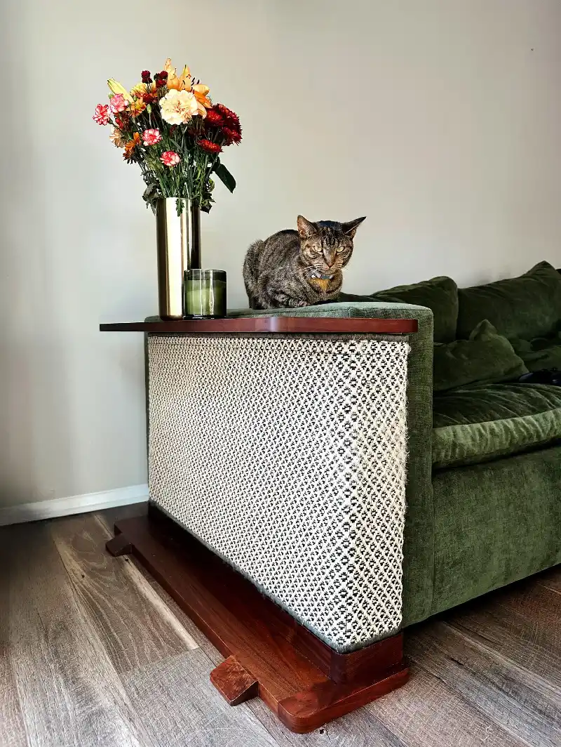 Woven Geometric Scratching Panel with Dark Wood Shelf Hugging a Green Velvet Sofa