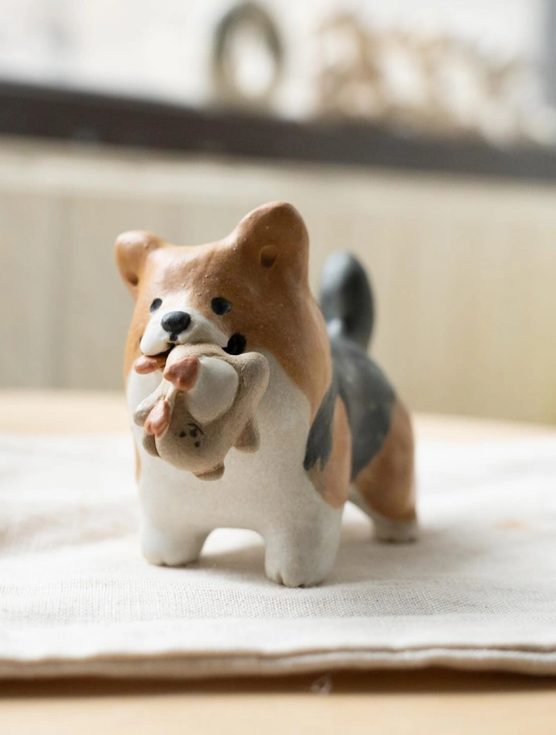 Ceramic Corgi Figurine Holding Toy on Linen Fabric