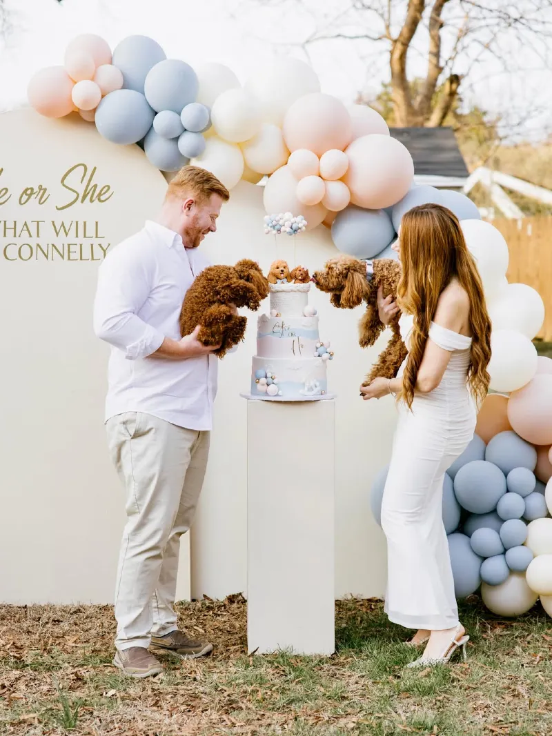 Couple Holding Poodles Next to a Tiered Cake and Balloon Arch