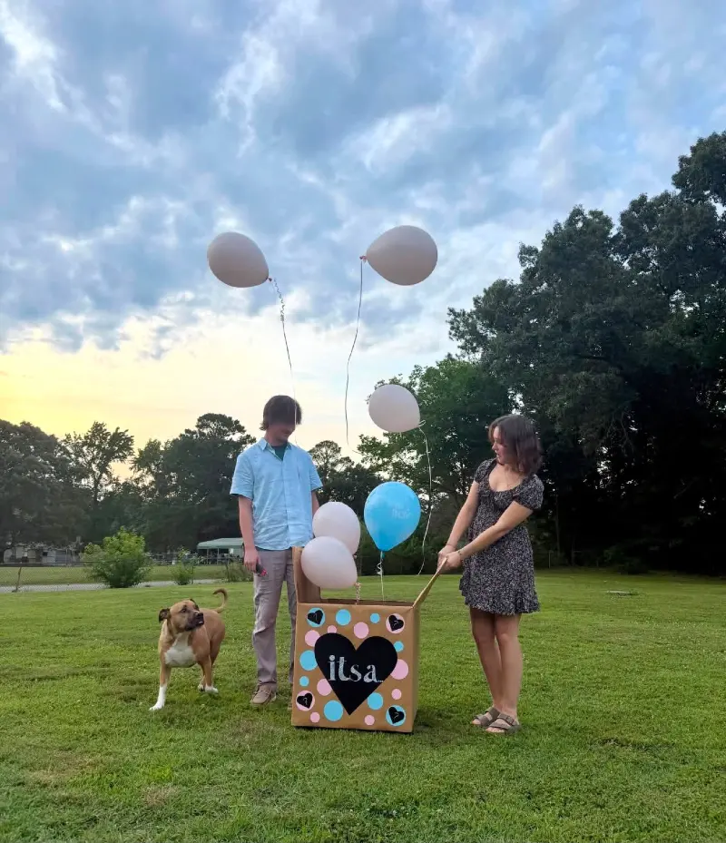 Couple Opening a Gender Reveal Balloon Box Outdoors with a Dog